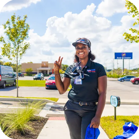 Smiling AquaShine Express Car Wash team member standing outside the car wash and waving at customers